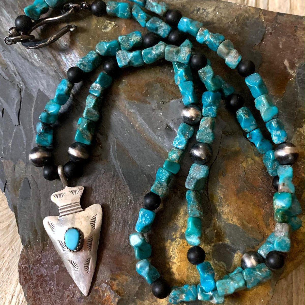 Turquoise beaded necklace with black and silver accents on a stone surface